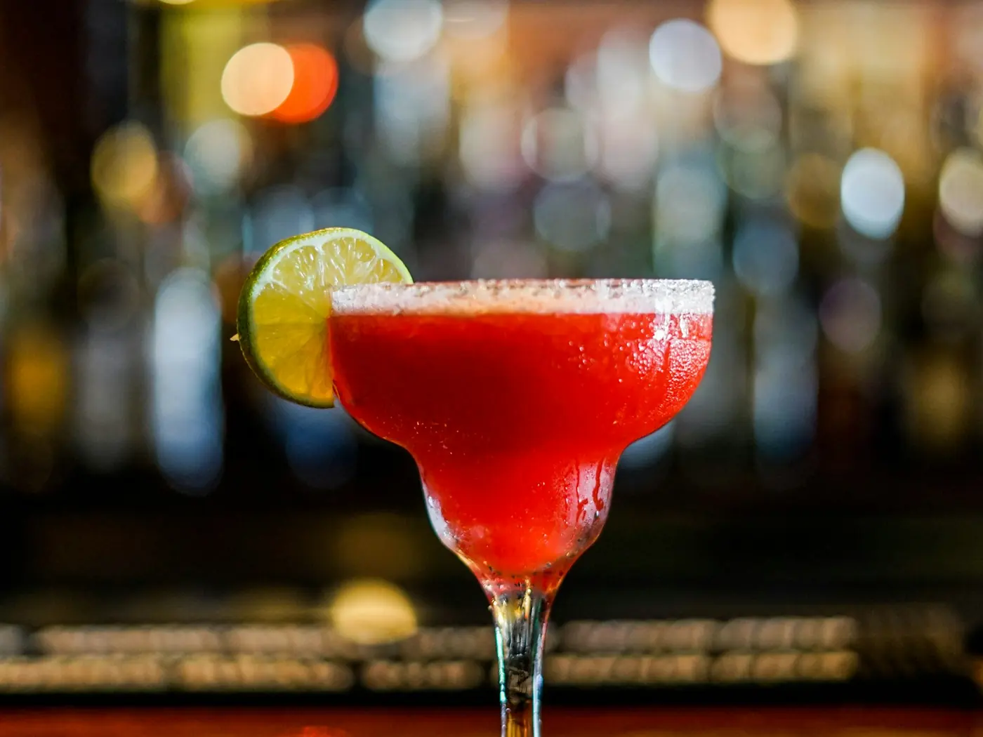 A red margarita with a salted rim and a lime wheel at a lit bar