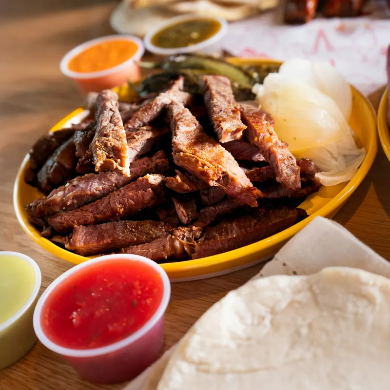 Sliced grilled steak on a yellow plate with red and green salsa and warm tortillas