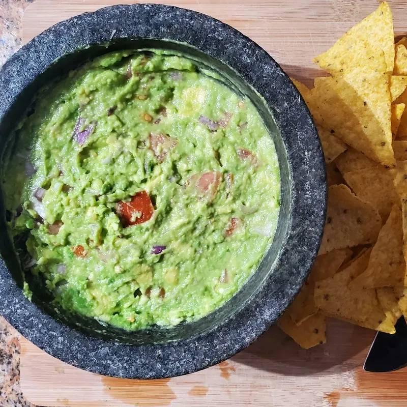 Guacamole in a stone molcajete beside tortilla chips