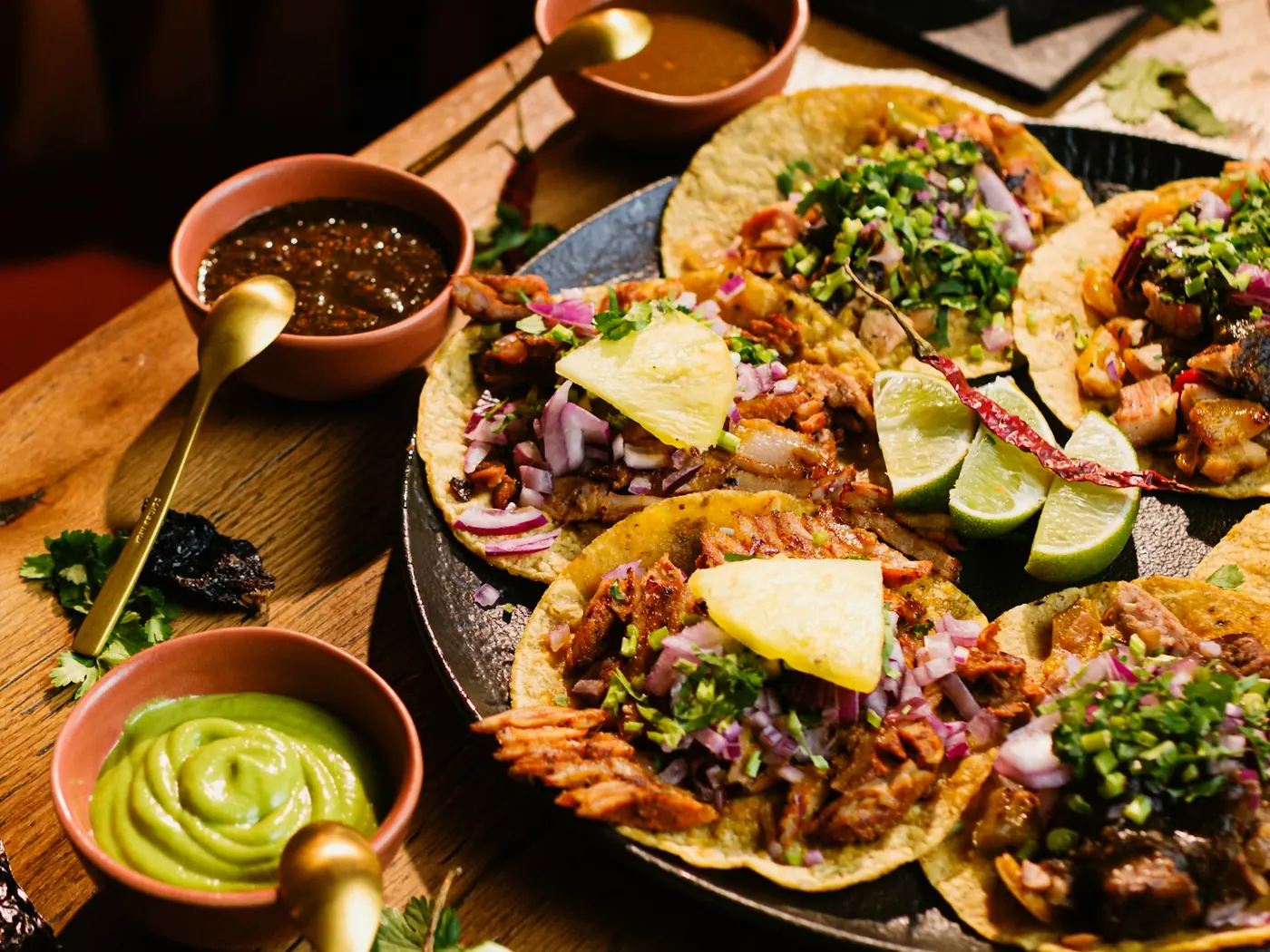 A platter of tacos with pineapple and lime, beside bowls of salsa