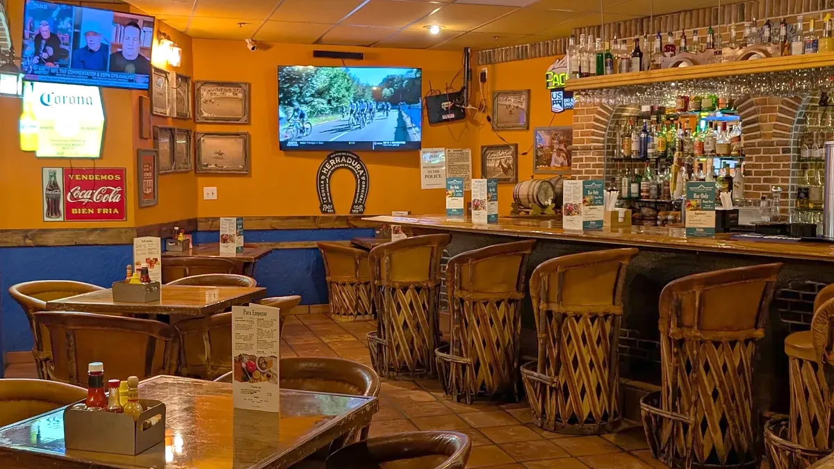 Leather stools at the bar, with shelves of bottles and a TV behind