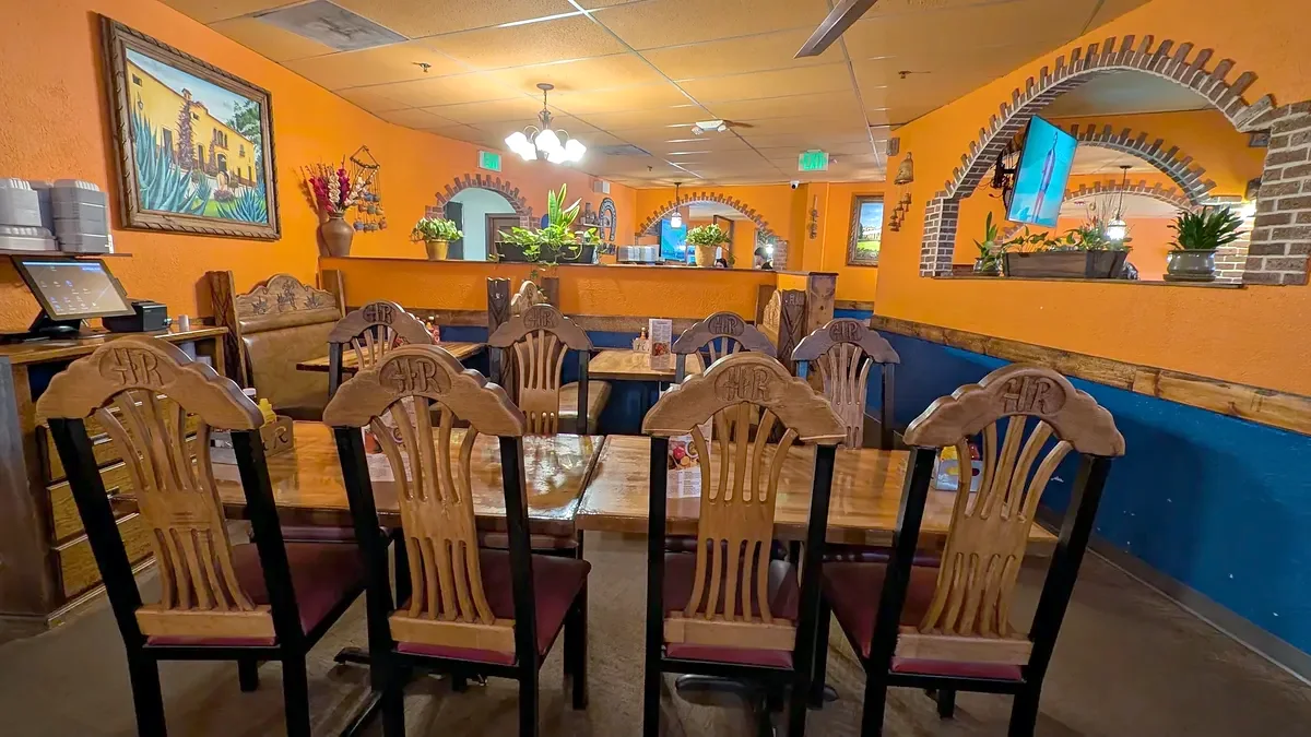 Four carved chairs at a wood table, brick arches along the orange wall
