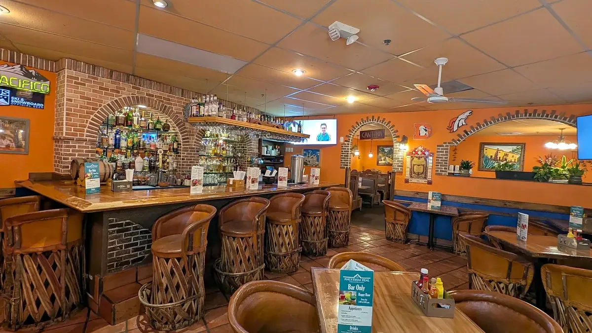 The bar from its end: a long wood counter, leather stools and a brick arch backbar