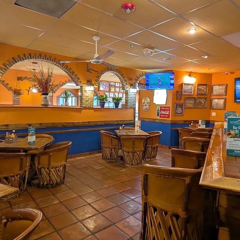 The end of the bar with brick arches behind it and leather stools on a tile floor